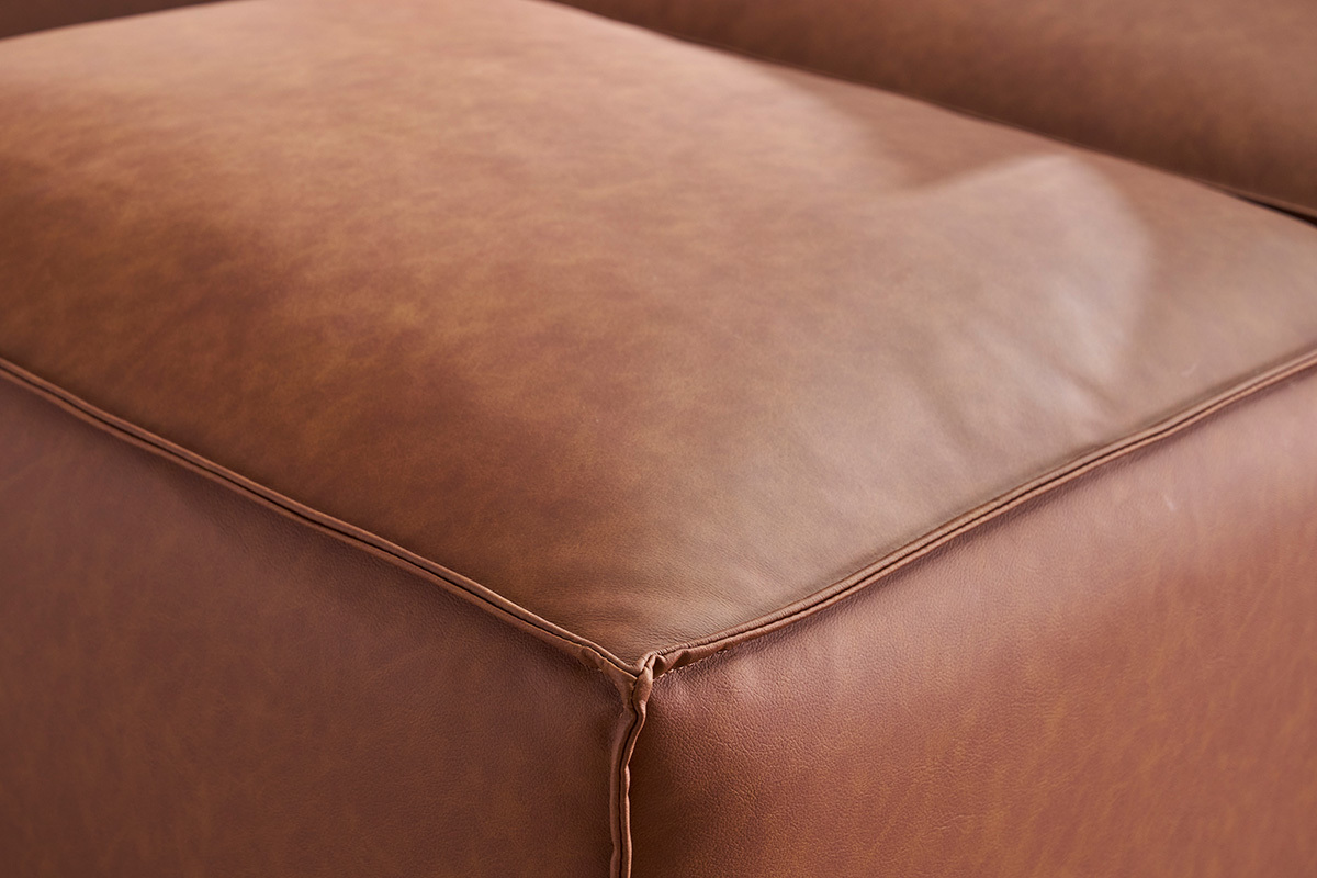 Vue rapproche d'un pouf en cuir marron avec coutures visibles.