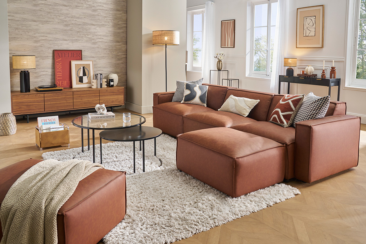 Salon avec canaps modulables en cuir brun, tables basses noires et tapis blanc.