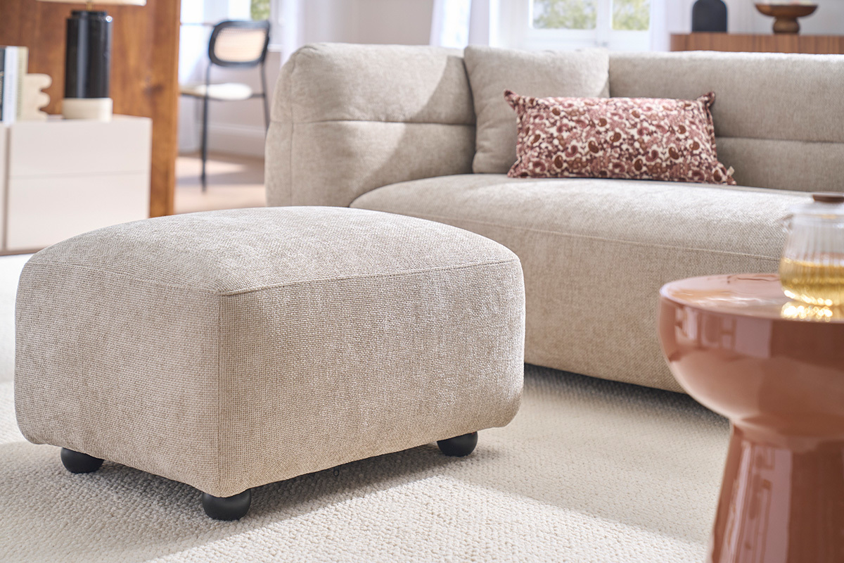 Pouf repose pieds en tissu beige, vue de c�t�, dans un salon moderne.