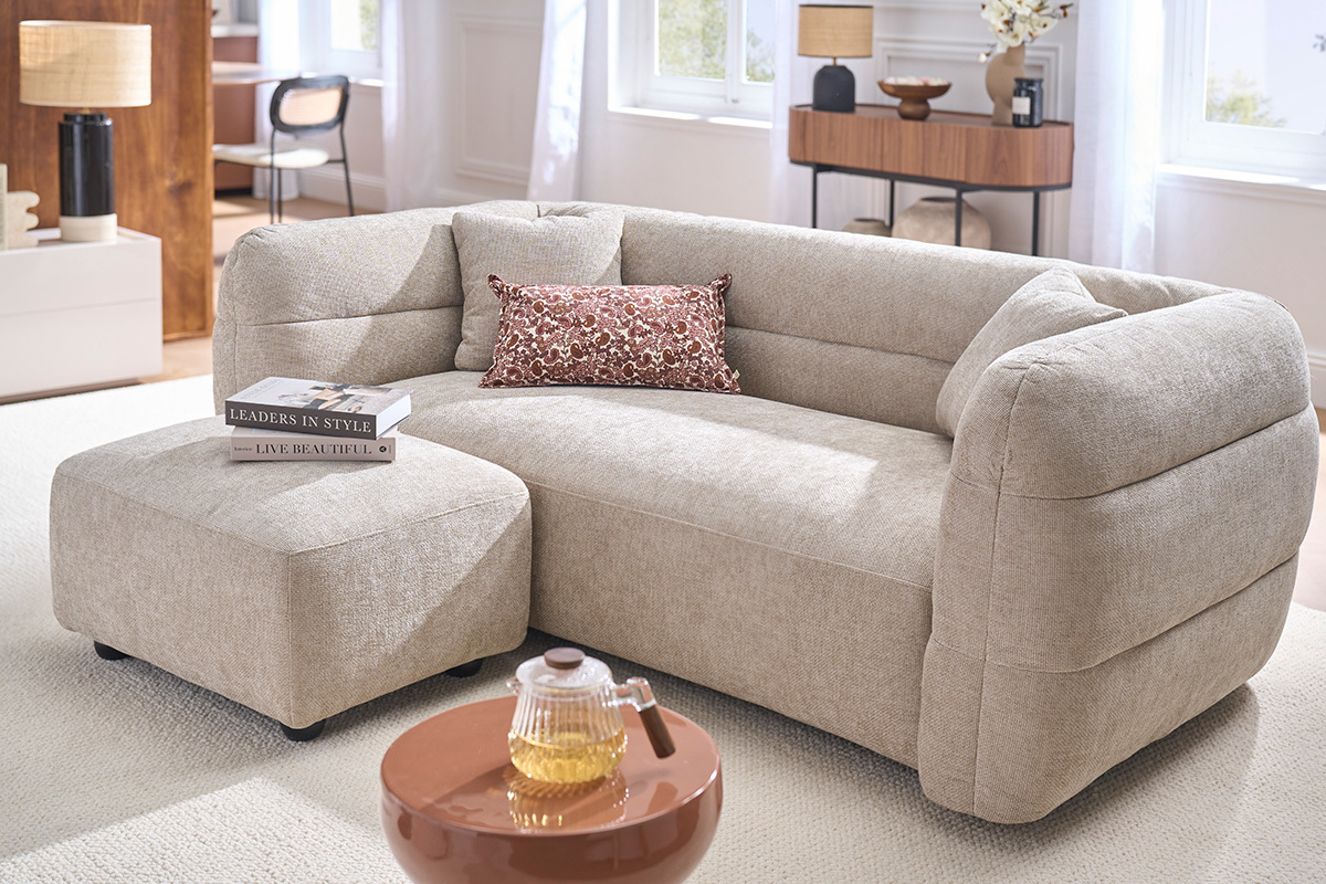 Pouf repose pieds en tissu beige, dans un salon moderne, pr�s d'un canap�.