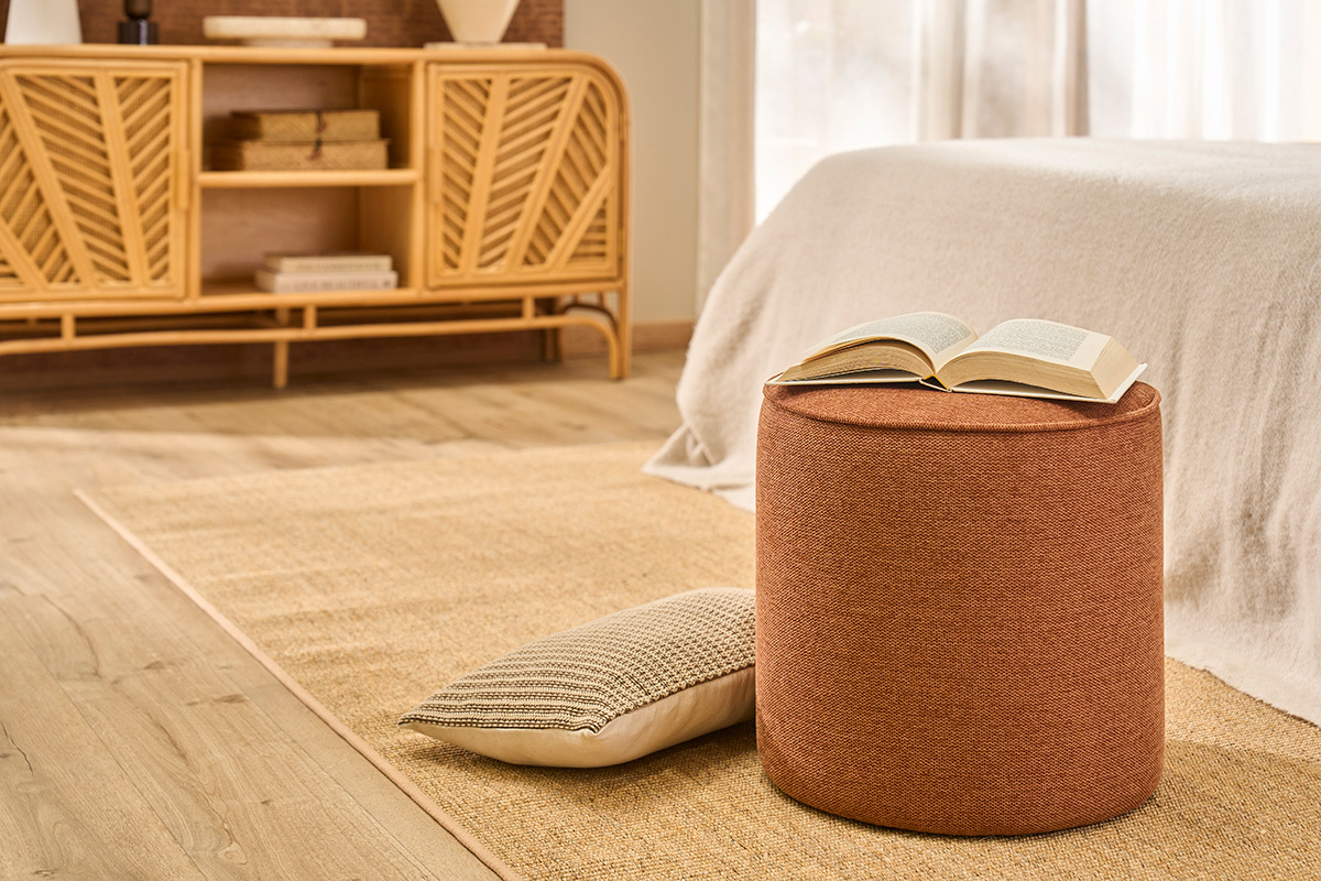 Pouf rond effet velours terre br�l�e avec livre ouvert, sur tapis beige.