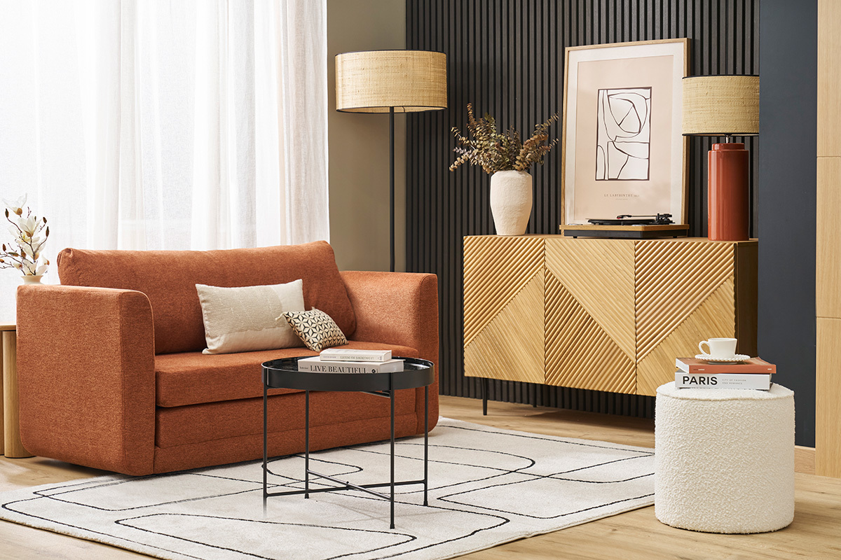 Salon moderne avec canap orange, table basse noire et pouf blanc  ct d'un meuble en bois.