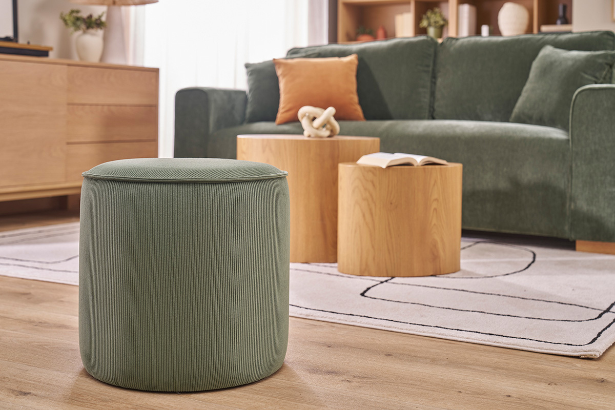 Pouf rond en velours c�tel� vert kaki devant un canap� vert.