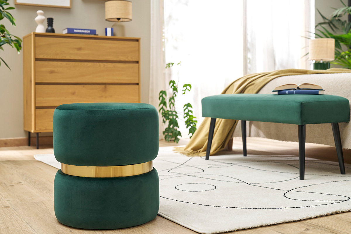 Pouf rond en velours vert fonc avec bande dore, pos dans un salon moderne.