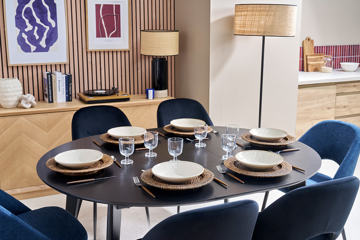 Table ronde extensible noire LEENA dresse pour 6, vue du dessus, entoure de chaises bleues.