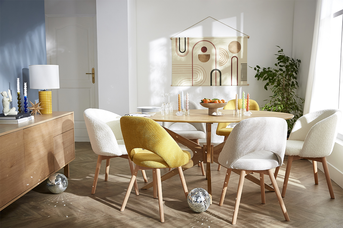 Table  manger ovale en noyer avec chaises colores dans une salle  manger lumineuse.