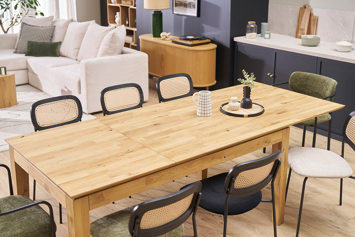 Table  manger extensible en chne clair entoure de chaises en rotin noir.