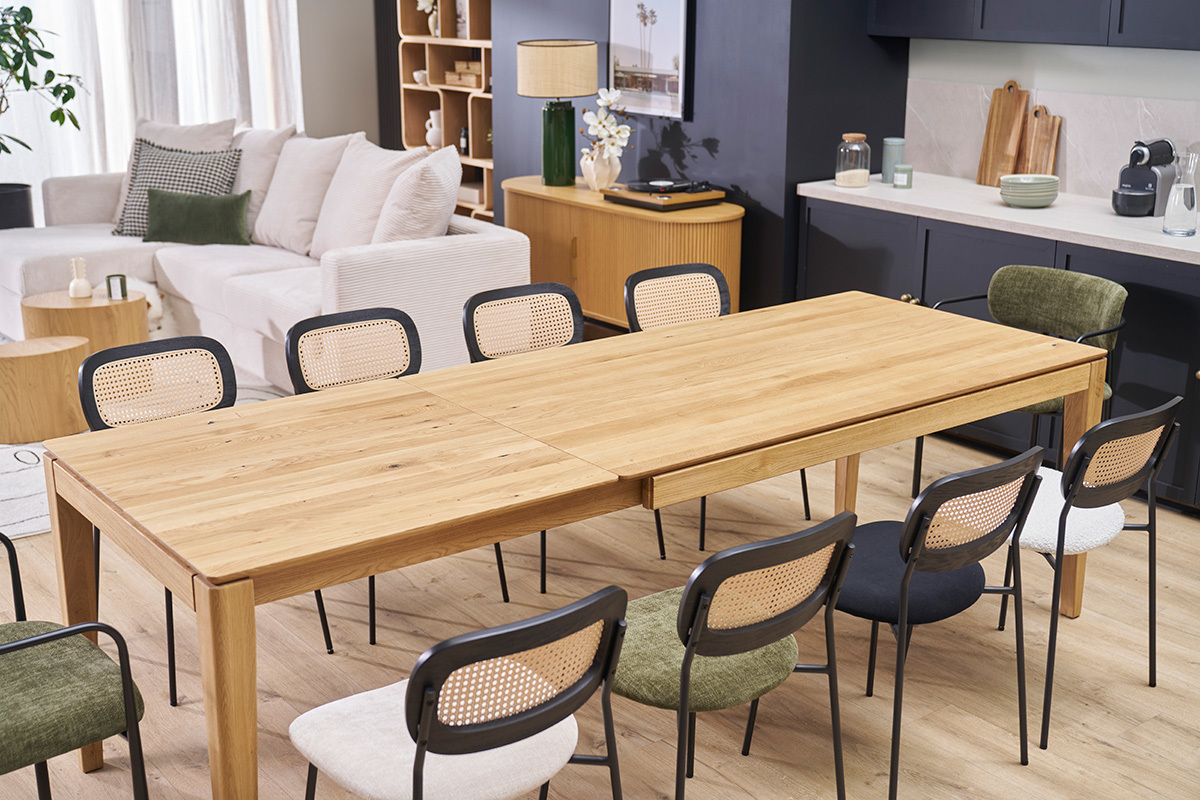 Table  manger extensible en chne clair avec chaises noires autour, vue en intrieur.