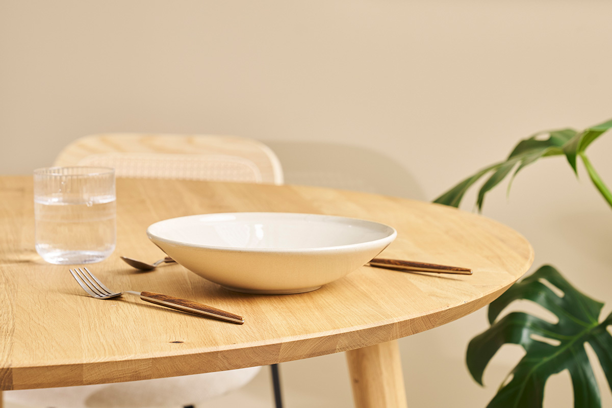 Table ronde en ch�ne clair avec assiette, verre et couverts, vue rapproch�e.