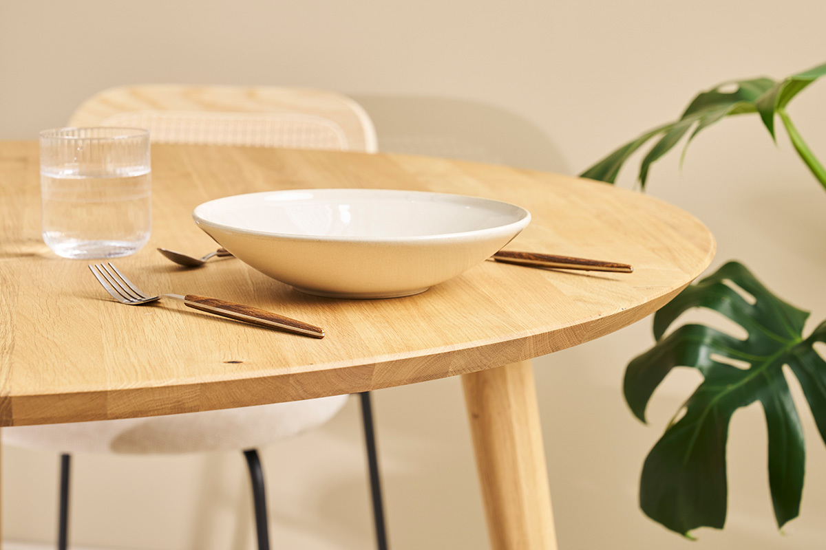 Table ronde en chne clair avec vaisselle et plante en arrire-plan, vue rapproche.