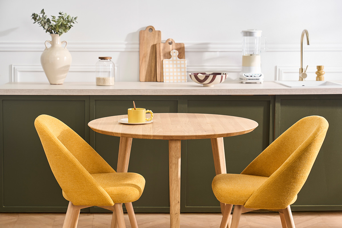 Table � manger ronde en ch�ne clair avec deux chaises jaunes dans une cuisine moderne.