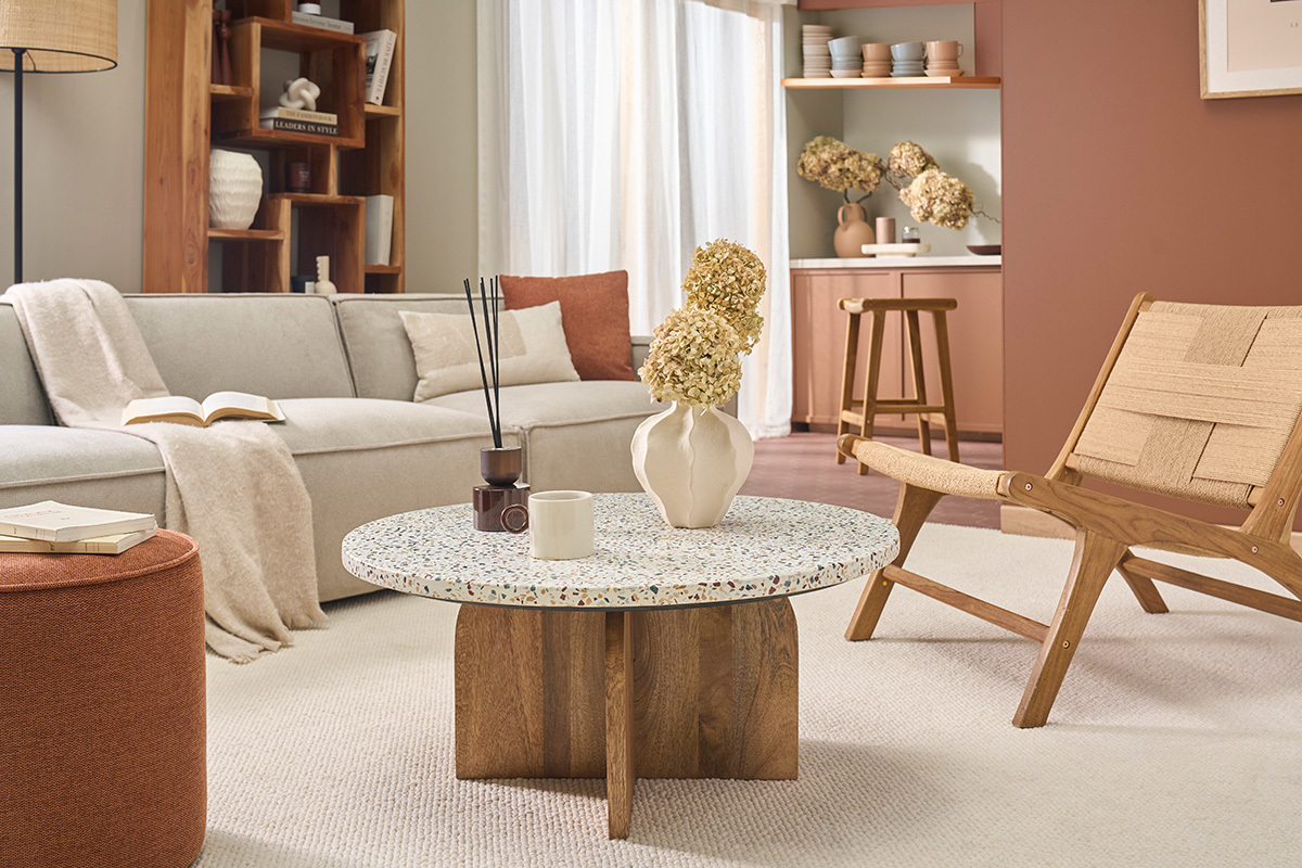 Table basse ronde en terrazzo et bois clair dans un salon moderne avec canap� et fauteuil.