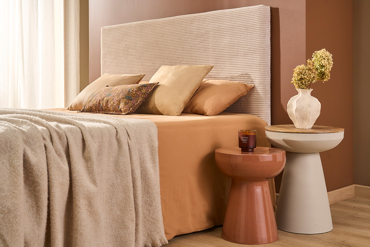 Table d'appoint ronde en m�tal terracotta pr�s d'un lit avec autres meubles.