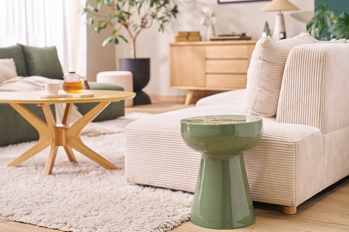 Table d'appoint ronde en m�tal �maill� vert kaki � c�t� d'un canap� beige, vue zoom�e.