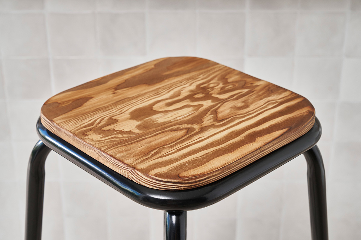 Gros plan sur l'assise carre en bois d'un tabouret de bar empilable avec structure en mtal noir.