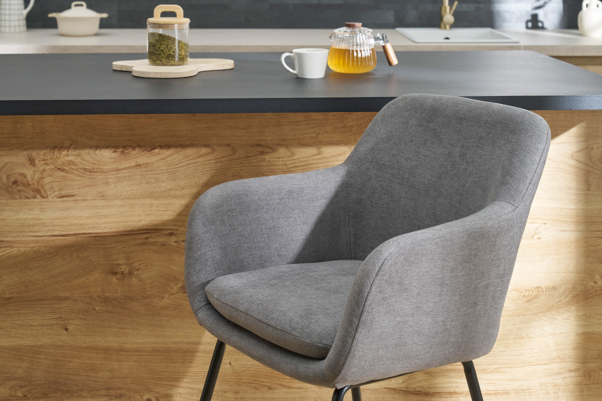 Tabouret de bar en tissu gris effet velours avec assise rembourre devant un comptoir en bois.