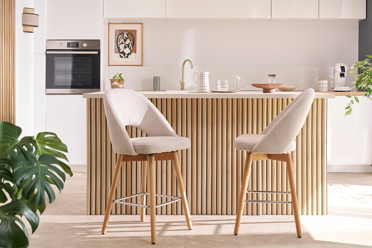 Tabourets de bar beiges en tissu avec pieds en h�v�a massif devant un comptoir de cuisine.