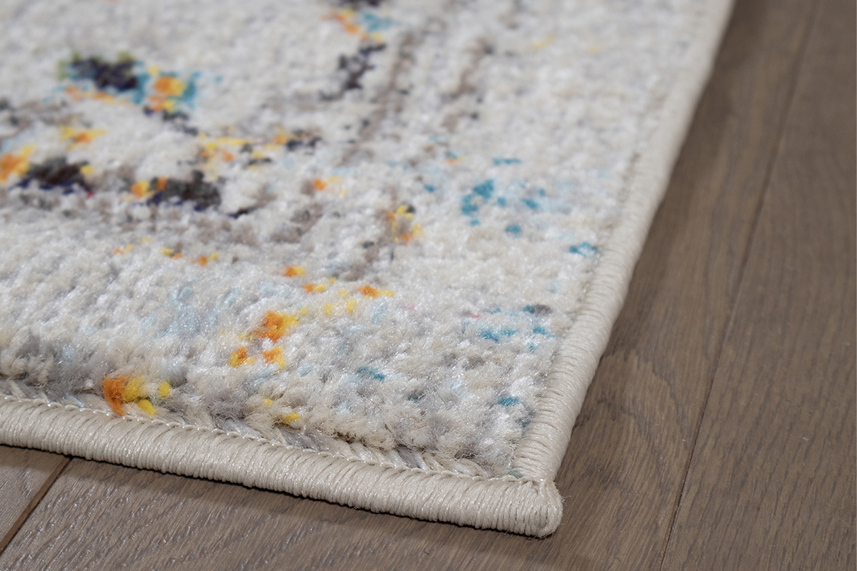 Tapis rectangulaire DULCE multicolore, vue en gros plan sur le motif et bordure sur sol en bois.