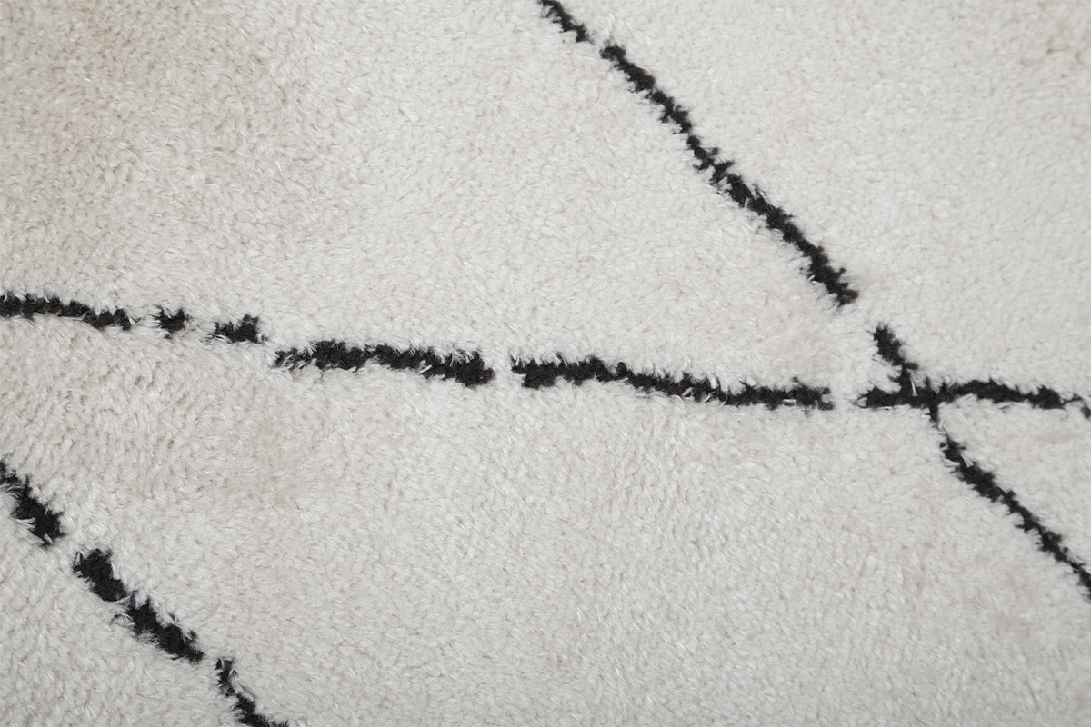 Gros plan sur un tapis � motifs losanges noirs sur fond blanc cass�.