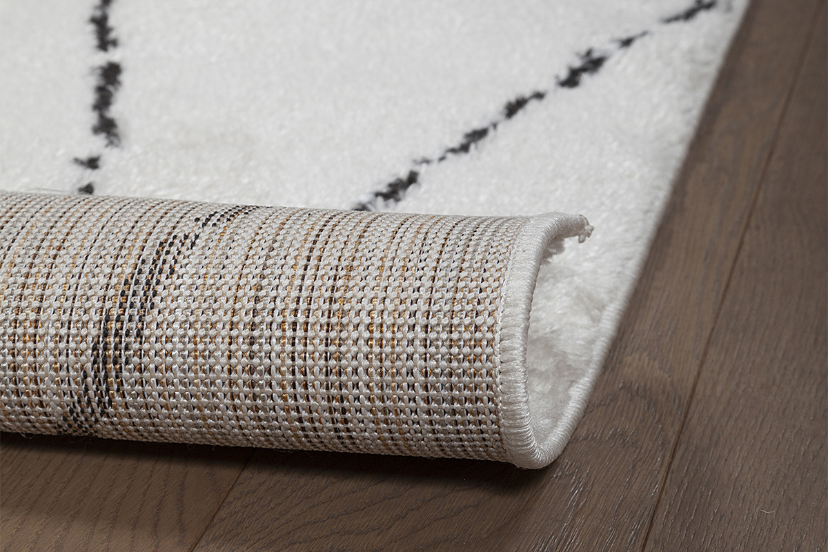 Gros plan sur le tapis SILAN avec motifs noirs et texture en tissu, partiellement roul�.