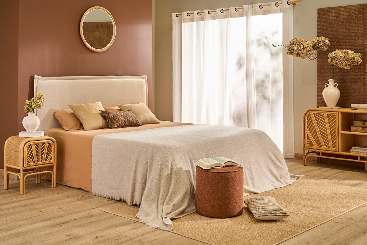 Chambre avec t�te de lit en tissu effet lin beige, lit double et meubles en rotin.